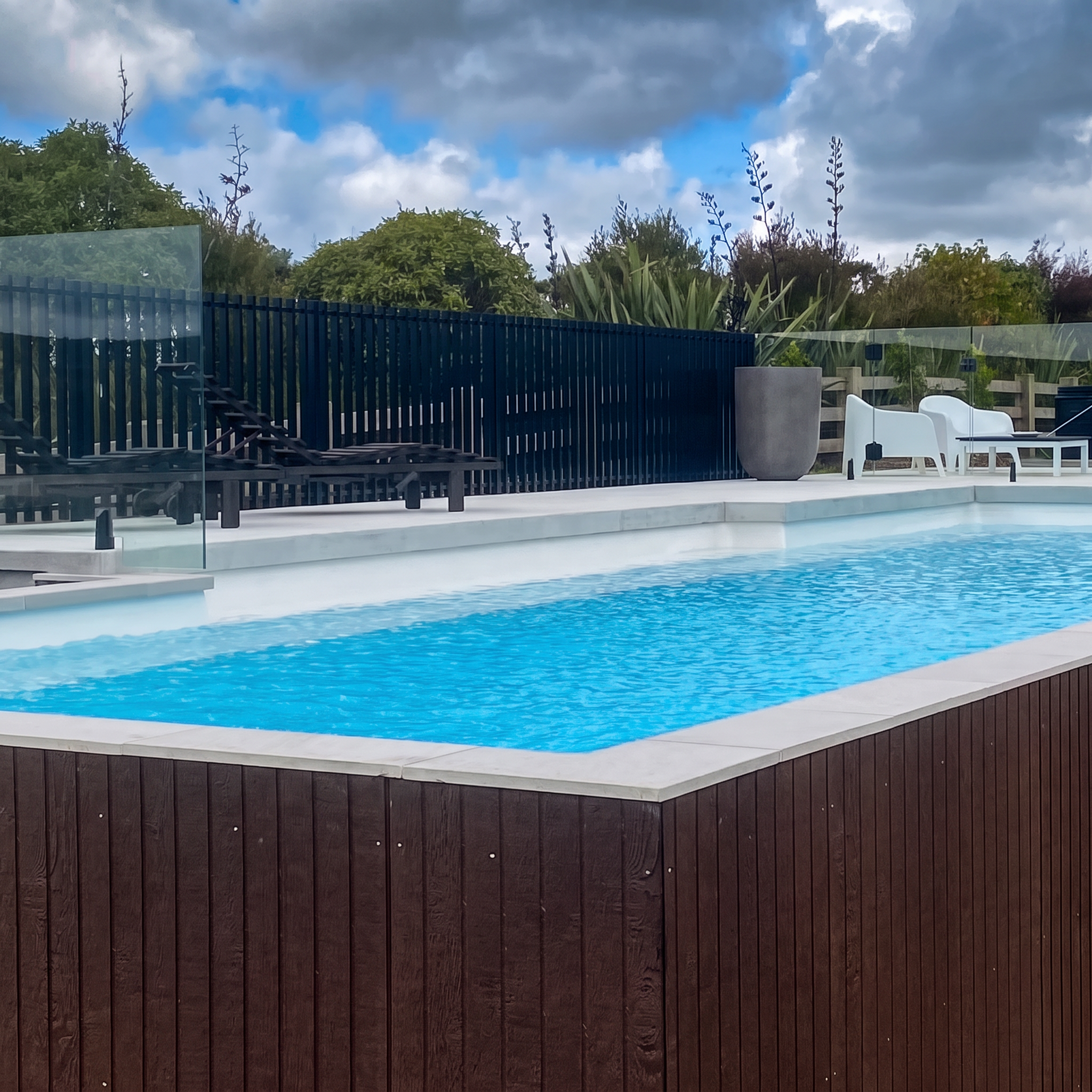 Pool with white coping, glass fencing and loungers